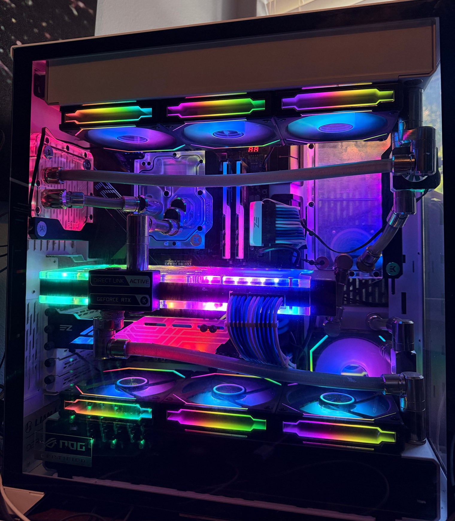 Full interior view of a white custom water-cooled PC with dark coolant tubing, clear CPU and graphics-card water blocks, and rows of rainbow-lit fans.