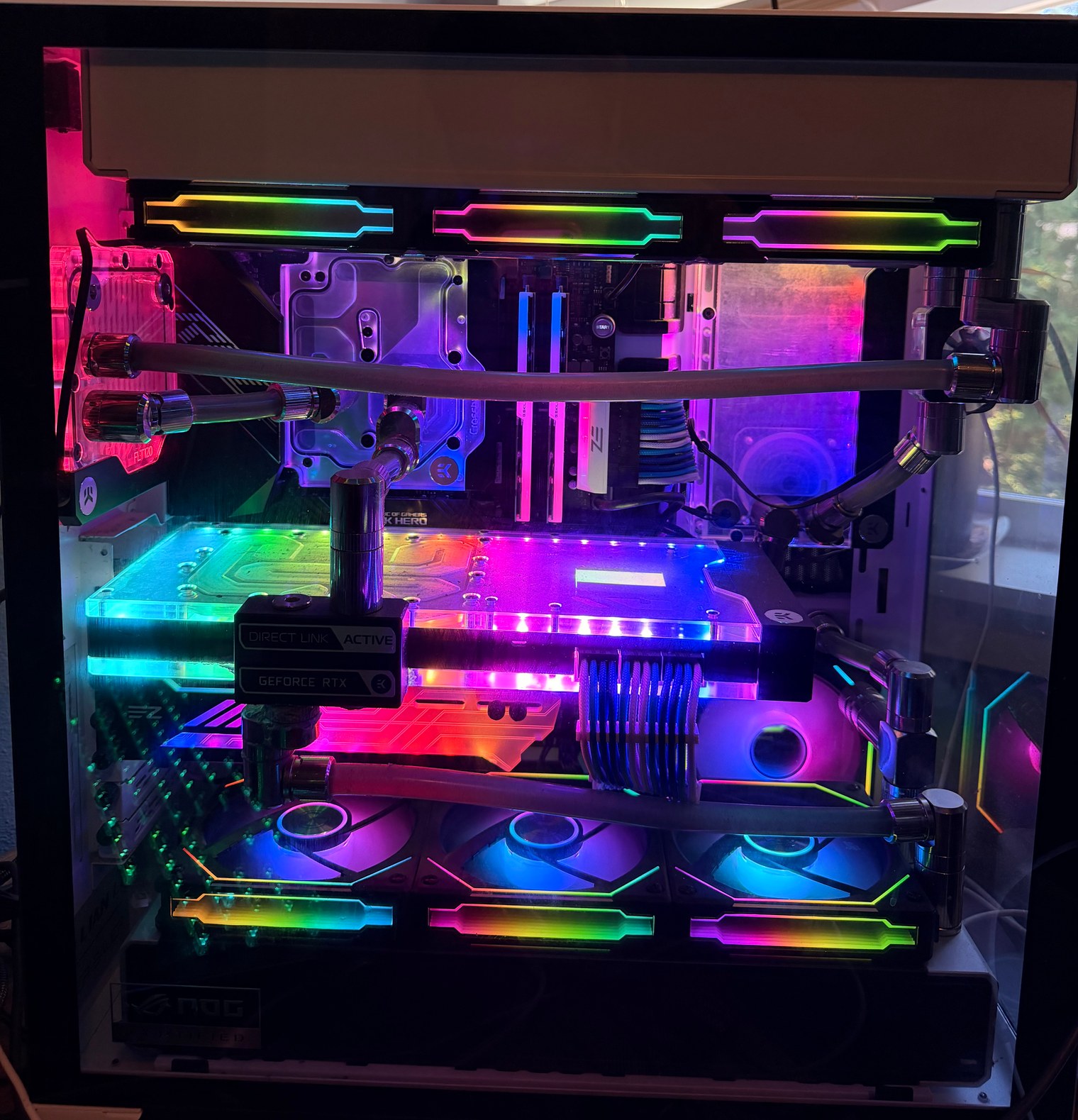 Closer interior view of the custom water-cooled PC showing dark coolant tubing, illuminated CPU and graphics-card blocks, RGB memory, and rainbow-lit fans.